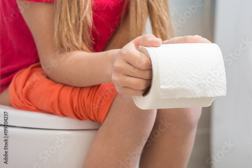 A girl is holding a roll of toilet paper in her hands, sitting on the toilet photo