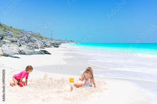 Adorable little kids play with sand on the white beach