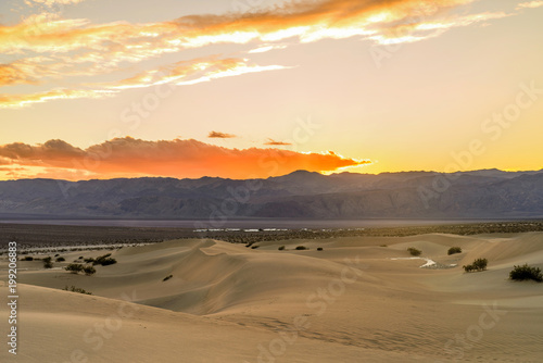 Sunset Sand Dunes - A colorful Spring sunset at Mesquite Flat Sand Dunes, with Stovepipe Wells village seen at base of Panamint Range. Death Valley National Park, California, USA. 