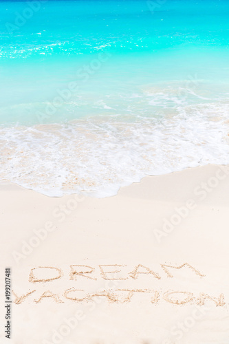 Dream written on sandy beach with soft ocean wave on background