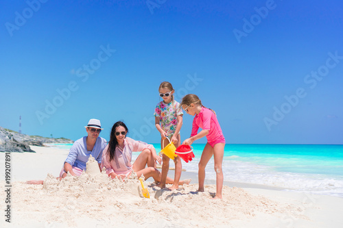 Family of four making sand castle at tropical white beach