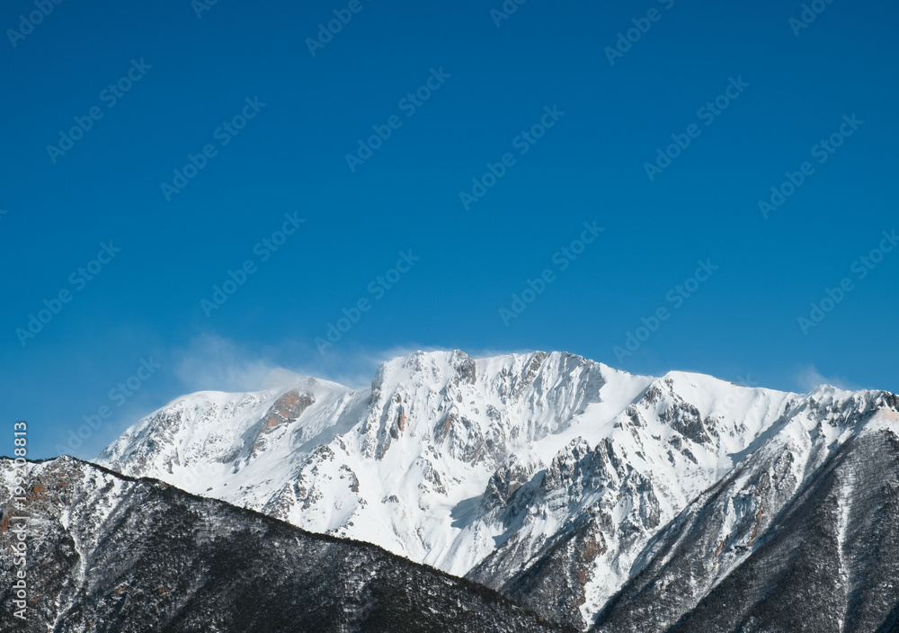 Karachay-Cherkessia mountain peaks in snow against the blue sky and green coniferous forest at the foot of the spring