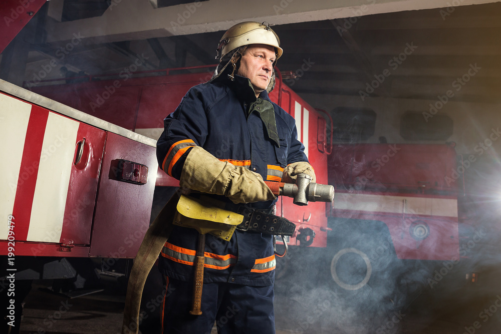 Fireman (firefighter) in action standing near a firetruck. Emergency safety. Protection, rescue from danger. Fireman (firefighter) in action standing near a firetruck. Emergency safety. Protection, rescue from danger.