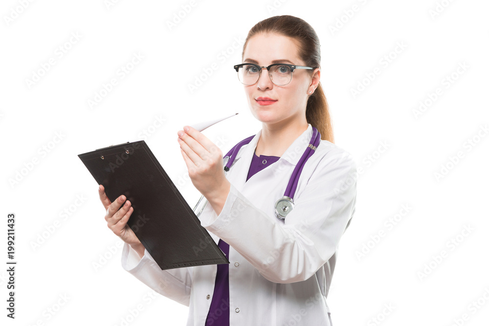 Attractive caucasian brunette female doctor standing in office with thermometer and clipboard in her hands on white background Attractive caucasian brunette female doctor standing in office with thermometer and clipboard in her hands on white background