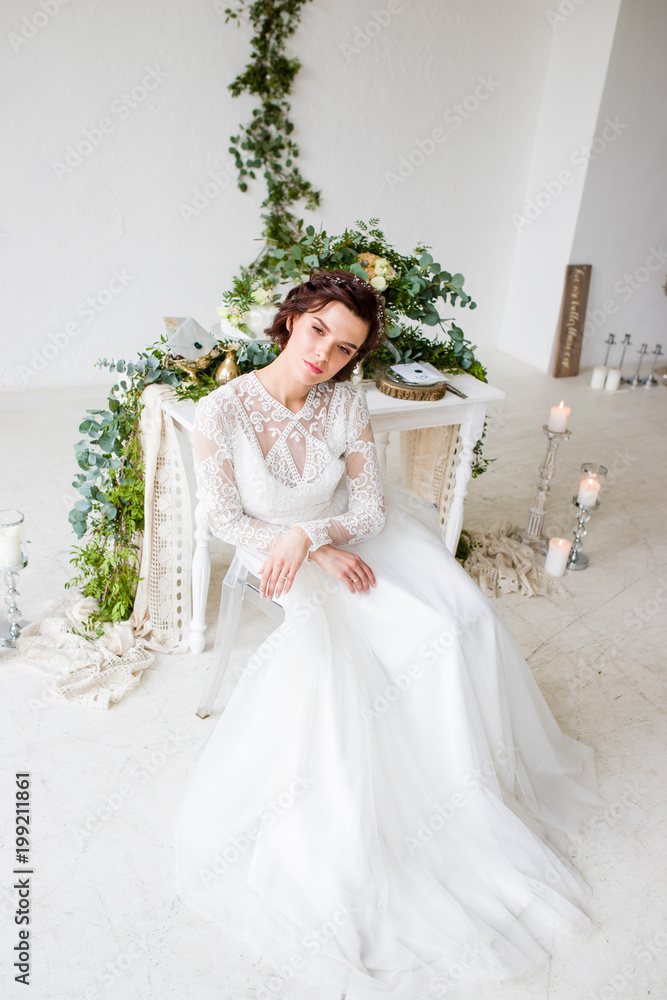 Beautiful wife sitting in a white room decorated with green decor in a botanical style