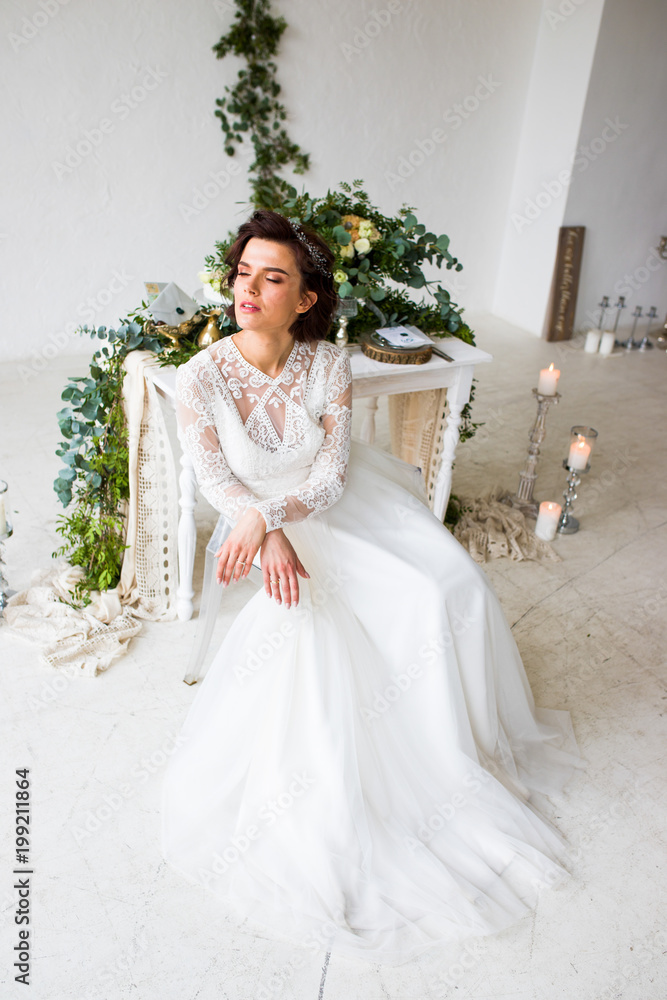 Fototapeta premium Beautiful model sitting in a white room decorated with green decor in a botanical style