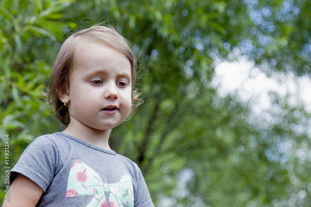 Cute llittle child girl outdoors against green leaves of trees Cute llittle child girl outdoors against green leaves of trees