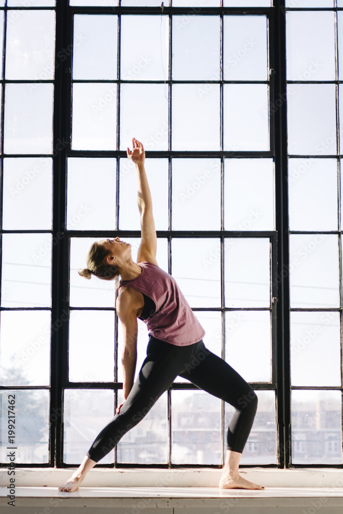 Female athlete practicing yoga by window in gym Female athlete practicing yoga by window in gym