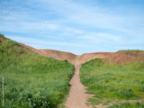 Path in grassy field leading to a dirt hill