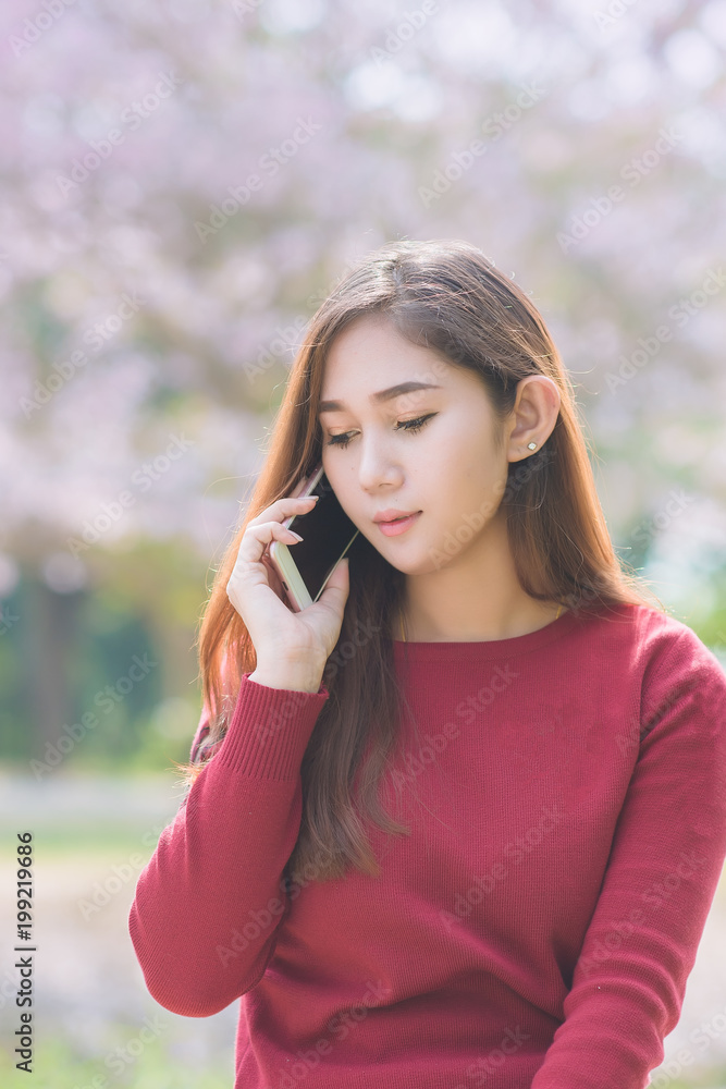 Portrait of pretty young asian woman use smartphone at park in autumn. Asian woman calling phone over flower background. Portrait of pretty young asian woman use smartphone at park in autumn. Asian woman calling phone over flower background.
