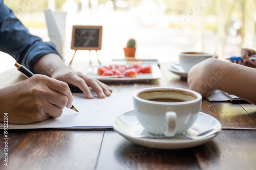 Men hand holding pen over agreement form with cup coffee