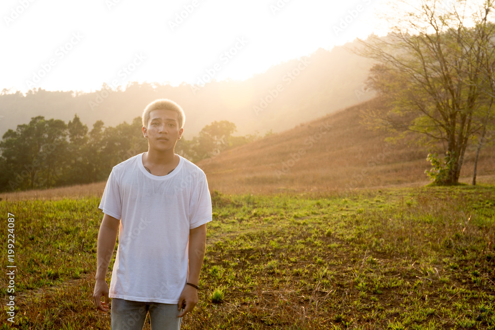 Young handsome asian man in white T-Shirt stands in a field