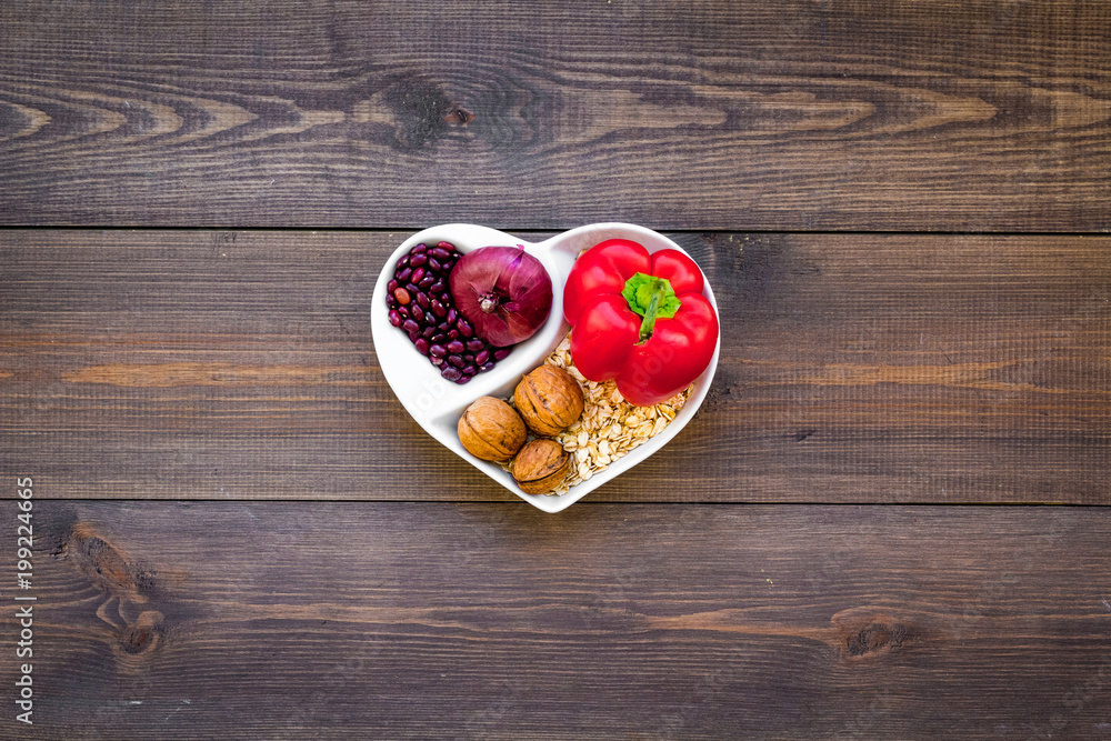 Food which help heart stay healthy. Vegetables, fruits, nuts in heart shaped bowl on dark wooden background top view copy space