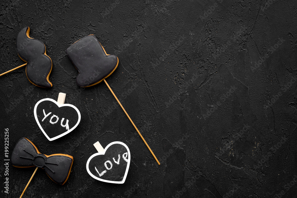 Men's birthday concept. Cookies in shape of moustache, hat, bow tie. Hearts with lettering love you on black background top view copy space