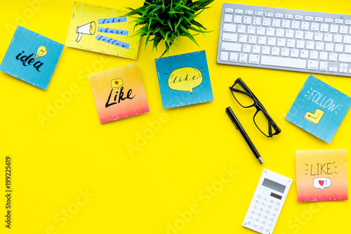 Socail media icons on work desk of marketing expert. Digital promotion of goods and services. Yellow background top view copy space