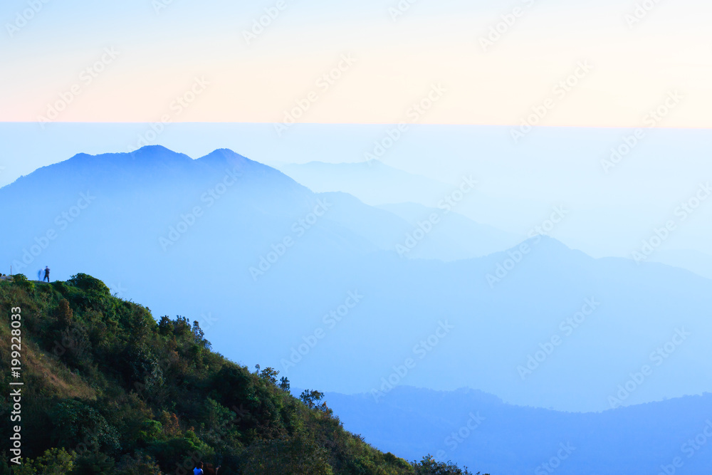 Hiker stands alone on the mountain peak at dusk.
