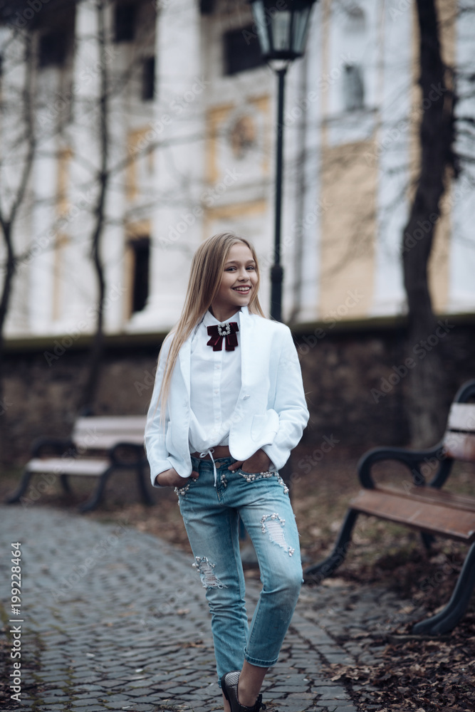 Girl smile in fashionable jeans in park, fashion. Little child with long blond hair outdoor, beauty. Baby beauty look and hairstyle. Happy childhood and youth. Kid fashion trend and style