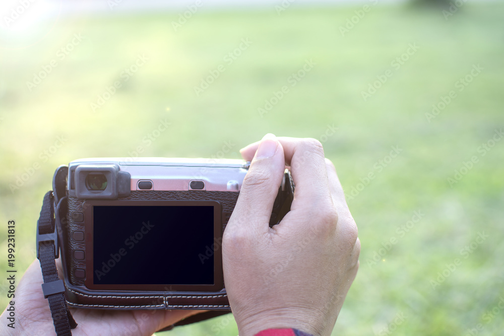 The digital DSLR camera in a woman hand. Blank screen of camera on female hand to take a photo in the green garden