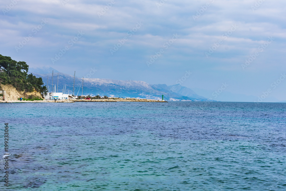 Beautiful Mediterranean landscape view of the coastline with a marina with sailing boats and mountains of Biokovo in the distance, over blue and turquoise sea water. Dalmatia region in Croatia