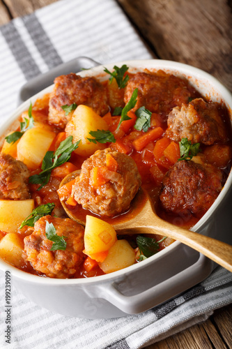Delicious tomato soup with meatballs and vegetables close-up in a saucepan. vertical