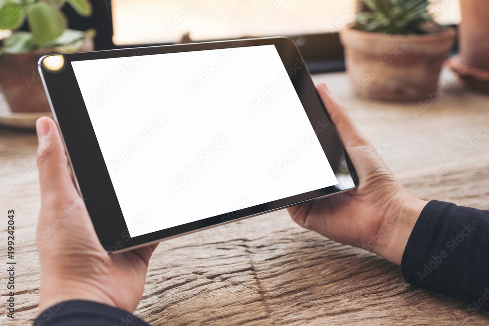 Mockup image of hands holding black tablet pc with blank white screen on vintage wooden table Mockup image of hands holding black tablet pc with blank white screen on vintage wooden table