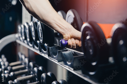 Close-up of man takes little dumbbell in gym.