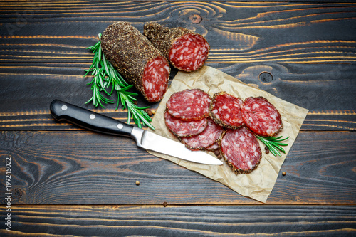 Dried organic salami sausage covered with pepper on wooden background