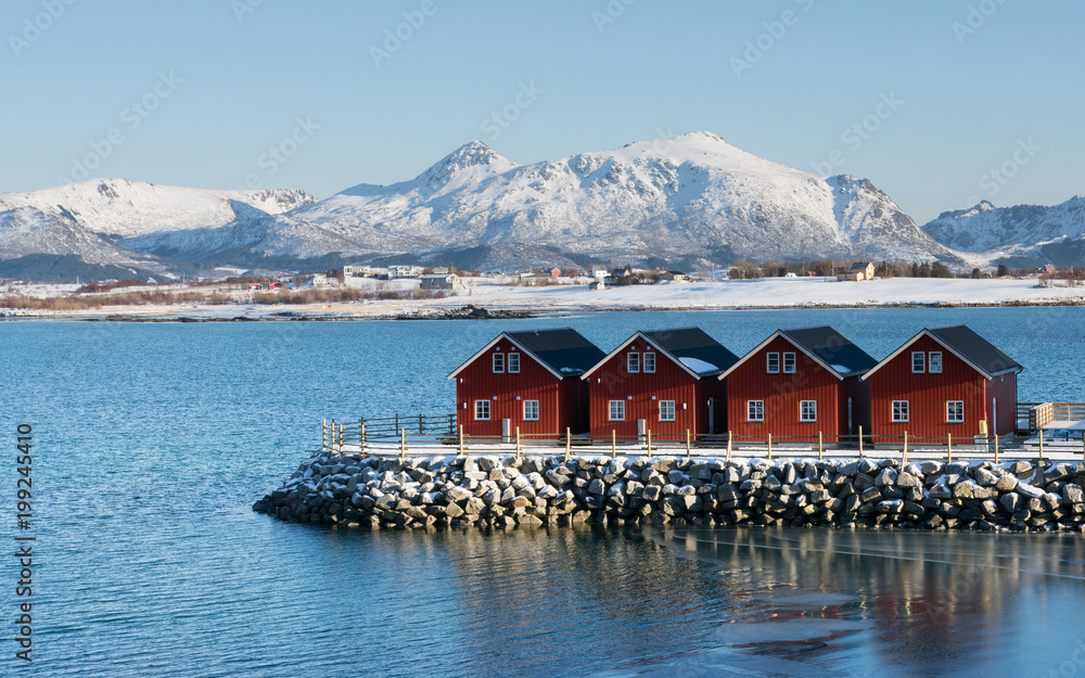typical norwegian red houses on stone pier with mountains in background