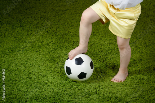 A little girl in shorts put her foot on a soccer ball on a green surface. Copyspace