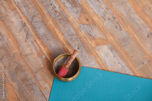 A diverse ethnic objects for meditation and relaxation: singing bowl, blue yoga or fitness mat on wiiden floor in yoga class photo