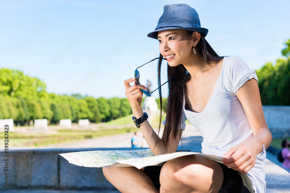 Asian young female tourist looking at camera while holding a map outdoors in the park