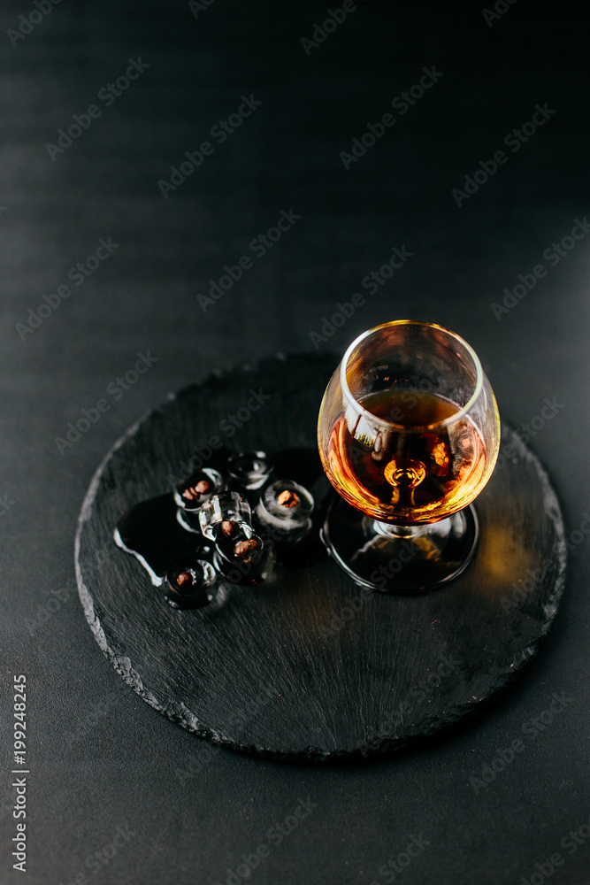 a glass of cognac on a black background, apperetiv with ice and coffee beans, view from above