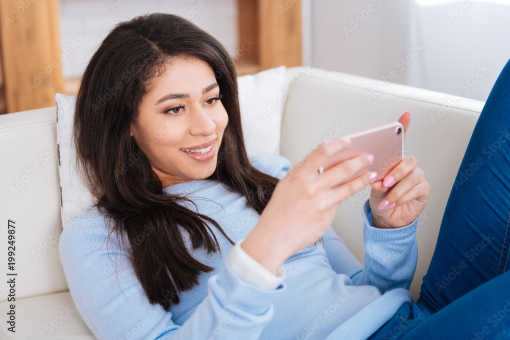 Useful tutorial. Happy exuberant woman lying on sofa while using smartphone Useful tutorial. Happy exuberant woman lying on sofa while using smartphone