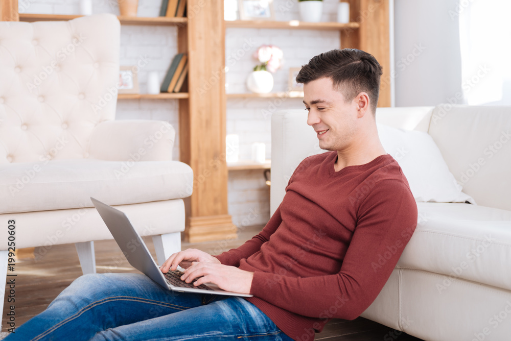 Online materials. Positive vigorous male student sitting in profile while typing on laptop Online materials. Positive vigorous male student sitting in profile while typing on laptop
