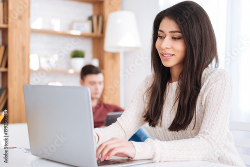 Many opportunities. Optimistic pretty female freelancer working on laptop and sitting at table