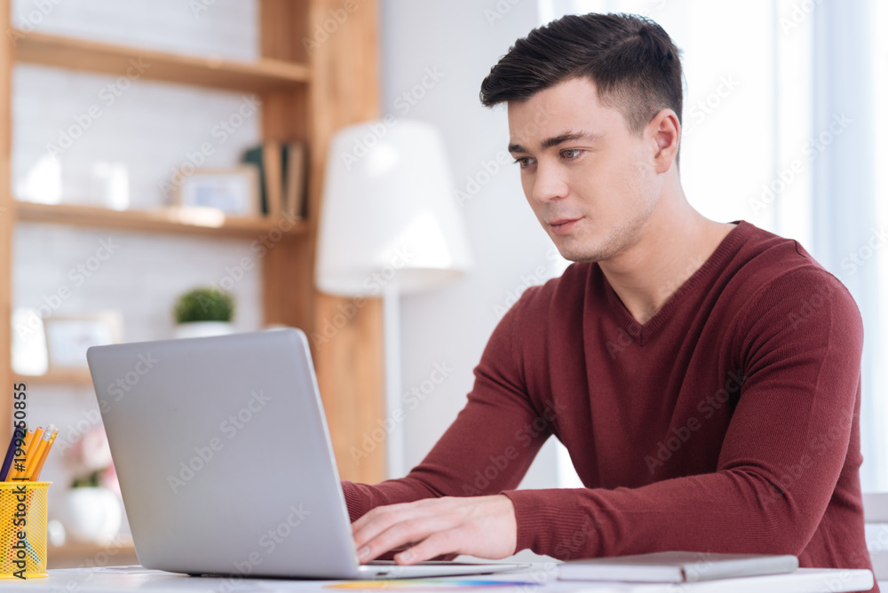 Work at home. Pleasant confident male freelancer typing on laptop while looking at screen Work at home. Pleasant confident male freelancer typing on laptop while looking at screen