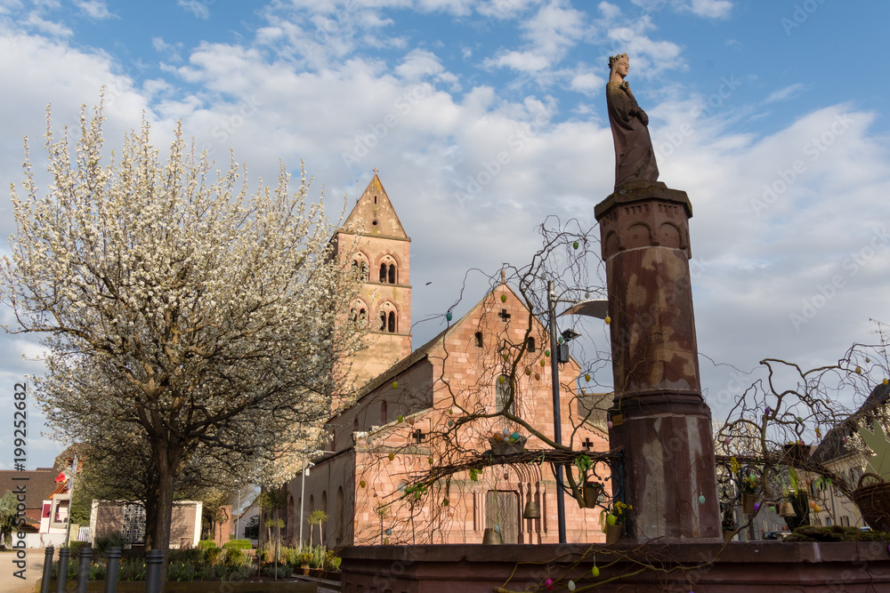 Statue de Sainte Richarde sur une fontaine en grès rose et ses décorations de Pâques, place de l’église de Sigolsheim, Kaysersberg vignoble, Alsace, France.