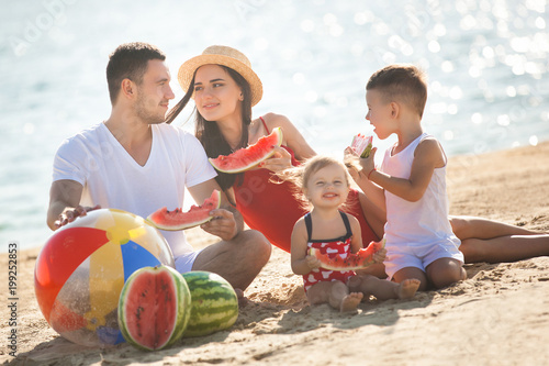 Cheerful family eating watermelon on the beach. Little kids and their parents on the sea shore having fun. Joyful family on the seaside