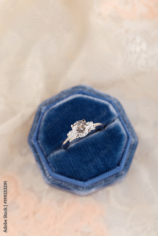 White golden wedding ring with diamonds in blue vintage velvet ring box on pink lace background White golden wedding ring with diamonds in blue vintage velvet ring box on pink lace background