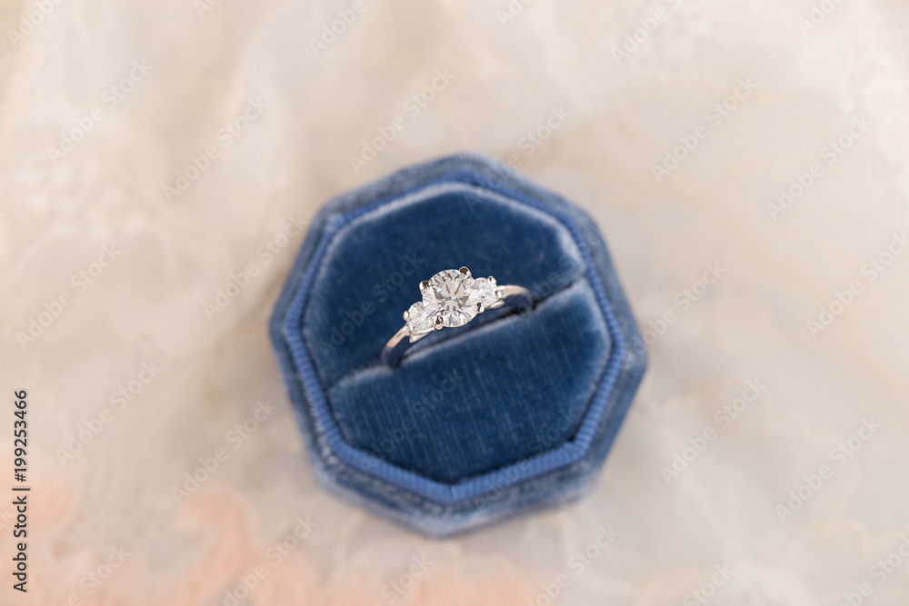 White golden wedding ring with diamonds in blue vintage velvet ring box on pink lace background White golden wedding ring with diamonds in blue vintage velvet ring box on pink lace background