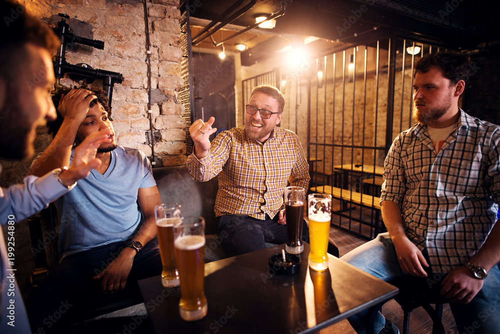 Cheerful smiling man showing wedding ring on his hand to confused friends while sitting in the pub. - obrazy, fototapety, plakaty 