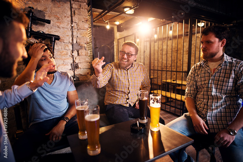 Cheerful smiling man showing wedding ring on his hand to confused friends while sitting in the pub.