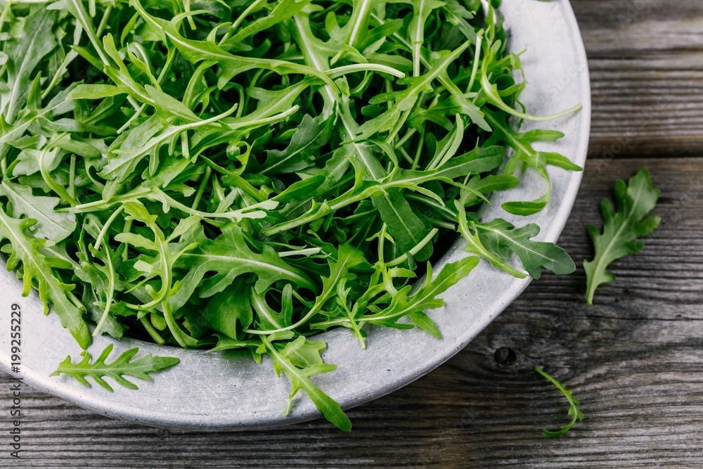 Fresh green arugula salad leaves in a bowl on a wooden background. Top view Fresh green arugula salad leaves in a bowl on a wooden background. Top view