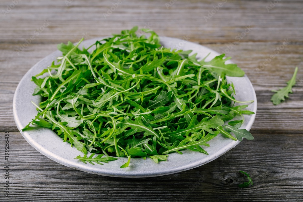 Fresh green arugula salad leaves in a bowl on a wooden background. Fresh green arugula salad leaves in a bowl on a wooden background.
