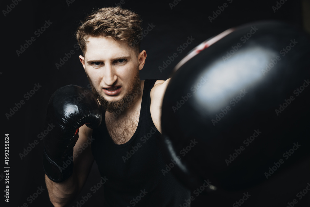 Angry sportsman with gloves on hands fighting and looking at camera on a black bakground.