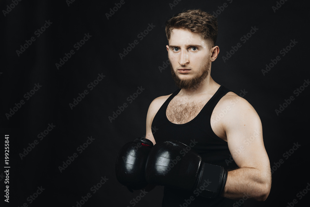 Young sportsman with gloves on hands looking seriously at camera on a black background.