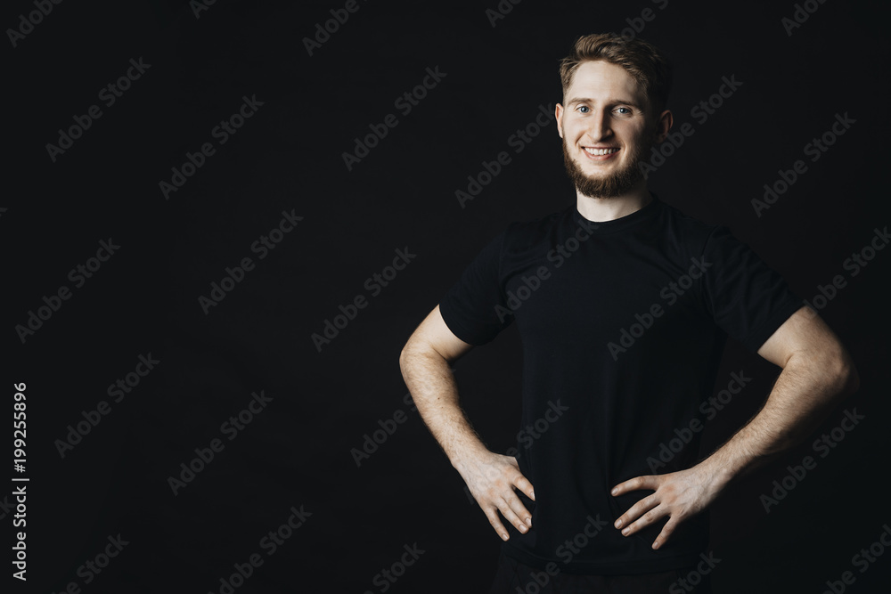 Sporty young man staying with hands on waist and smiling at camera.