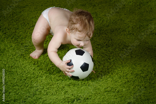 The kid takes a soccer ball on the green surface. Active games with children.