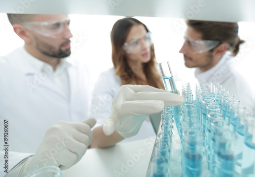 background image is a group of scientists studying the liquid in the glass tube.
