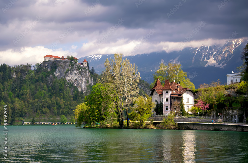 Scenic view of Lake Bled with castle, villas and mountains covered by clouds on background at springtime, Slovenia
